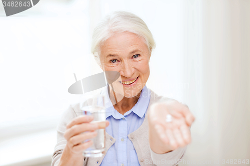 Image of happy senior woman with water and medicine at home