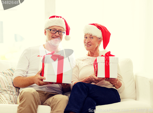 Image of happy senior couple in santa hats with gift boxes