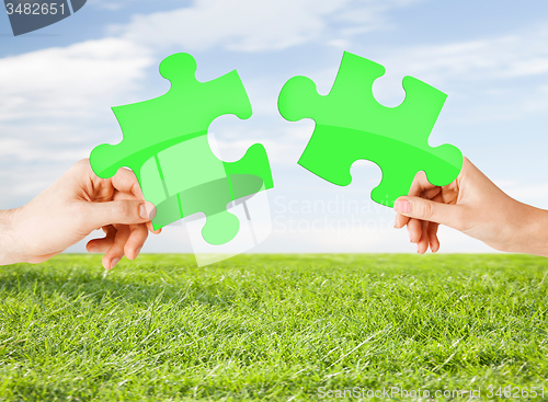 Image of hands with green puzzle over natural background