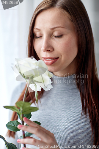 Image of happy woman smelling big white rose at home