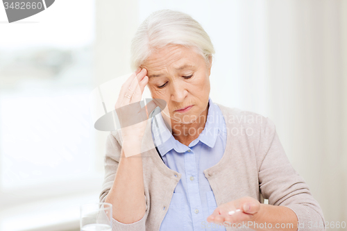 Image of senior woman with water and medicine at home