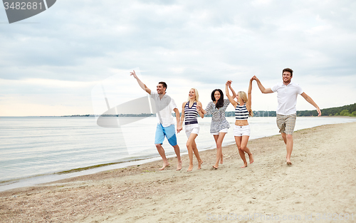Image of smiling friends in sunglasses walking on beach