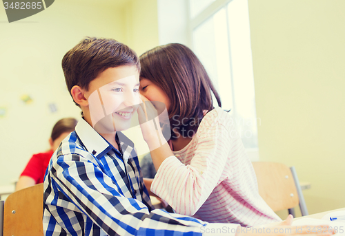 Image of smiling schoolgirl whispering to classmate ear