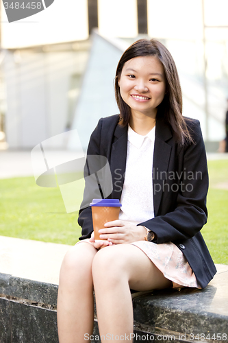 Image of Young female Asian executive drinking coffee