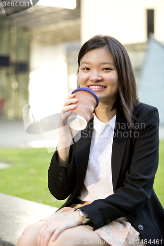 Image of Young female Asian executive drinking coffee