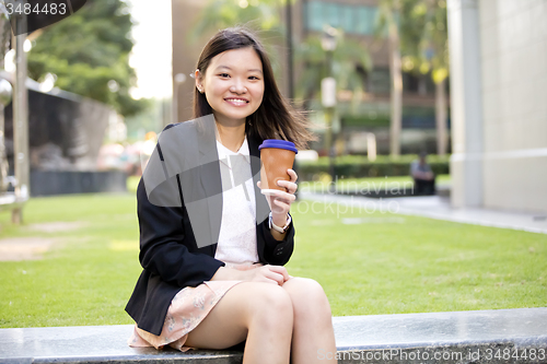 Image of Young female Asian executive drinking coffee