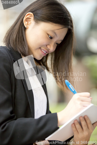 Image of Young Asian female business executive writing on notepad