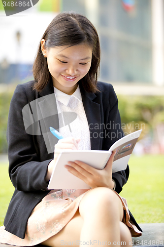 Image of Young Asian female business executive writing on notepad