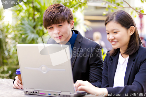 Image of Young Asian female and male business executive using laptop