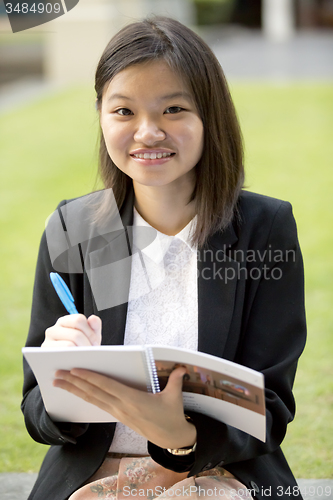 Image of Young Asian female business executive writing on notepad