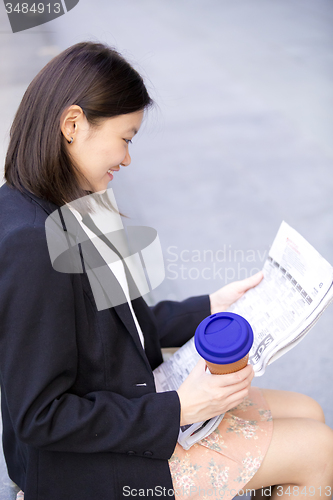 Image of Young Asian female business executive reading newspaper