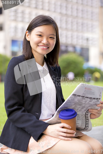 Image of Young Asian female business executive reading newspaper