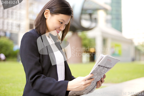 Image of Young Asian female business executive reading newspaper