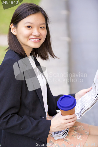 Image of Young Asian female business executive reading newspaper