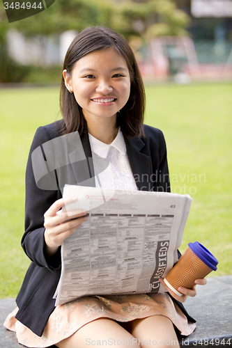 Image of Young Asian female business executive reading newspaper