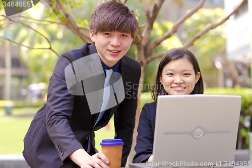 Image of Young Asian female and male business executive using laptop