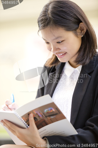 Image of Young Asian female business executive writing on notepad