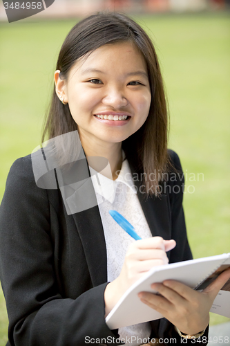 Image of Young Asian female business executive writing on notepad