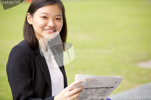Image of Young Asian female business executive reading newspaper