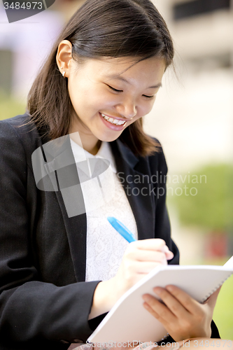 Image of Young Asian female business executive writing on notepad