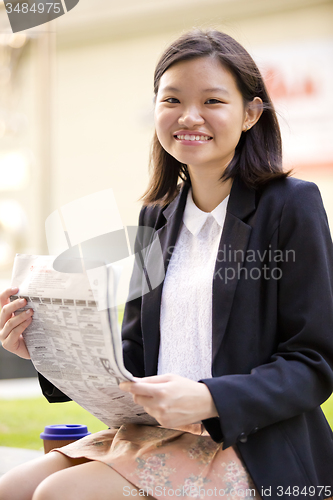 Image of Young Asian female business executive reading newspaper