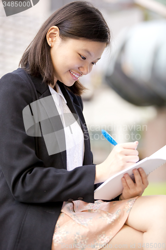 Image of Young Asian female business executive writing on notepad