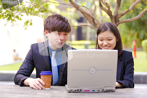 Image of Young Asian female and male business executive using laptop