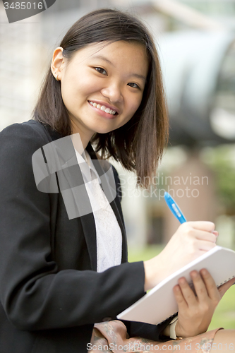 Image of Young Asian female business executive writing on notepad