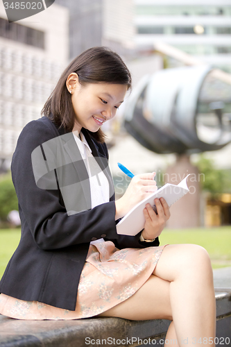 Image of Young Asian female business executive writing on notepad