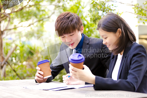 Image of Young Asian female and male business executive reading newspaper