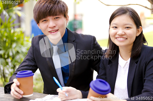 Image of Young Asian female and male business executive reading newspaper