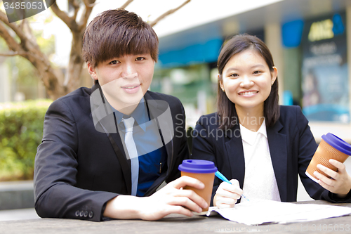 Image of Young Asian female and male business executive reading newspaper