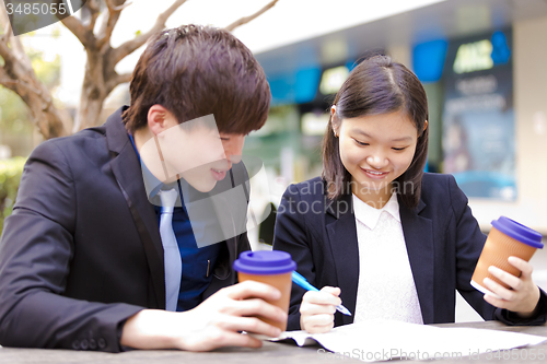 Image of Young Asian female and male business executive reading newspaper