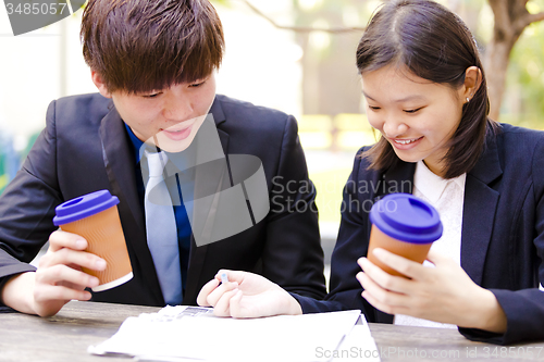 Image of Young Asian female and male business executive reading newspaper