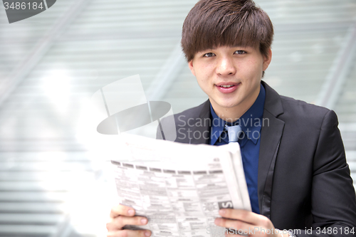 Image of Young Asian business executive reading newspaper