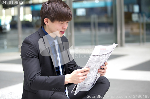 Image of Young Asian male business executive reading newspaper