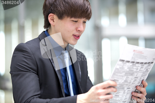 Image of Young Asian male business executive reading newspaper