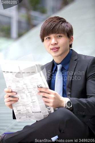 Image of Young Asian male business executive reading newspaper