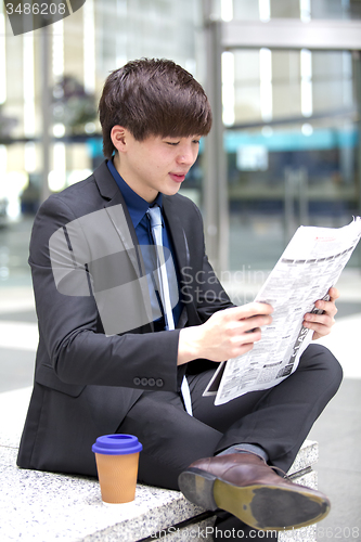 Image of Young Asian male business executive reading newspaper