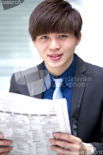 Image of Young Asian male business executive reading newspaper