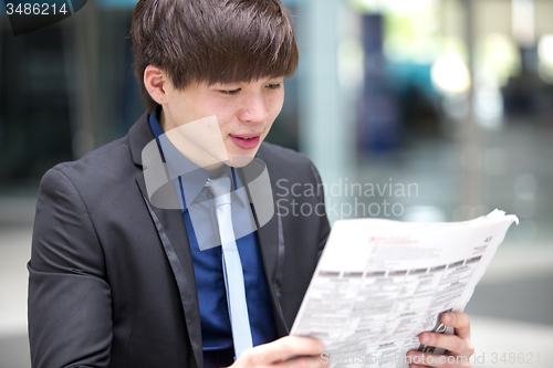 Image of Young Asian male business executive reading newspaper