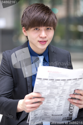 Image of Young Asian male business executive reading newspaper