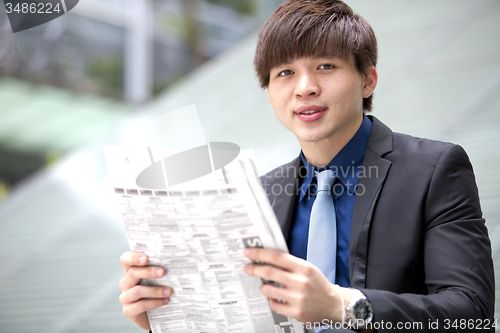 Image of Young Asian male business executive reading newspaper