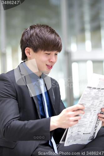 Image of Young Asian male business executive reading newspaper