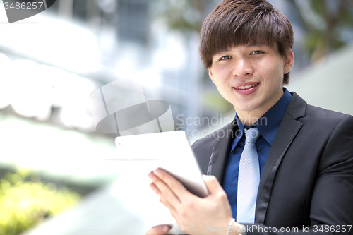 Image of Young Asian business executive in suit holding tablet and coffee