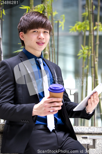 Image of Young Asian business executive in suit holding tablet and coffee