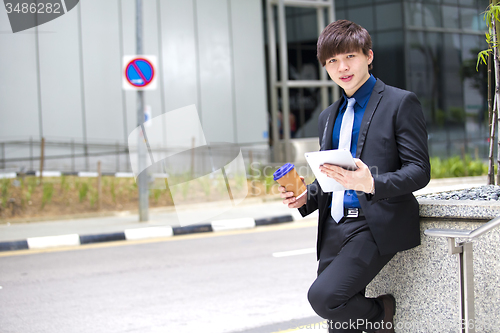 Image of Young Asian business executive in suit holding tablet and coffee