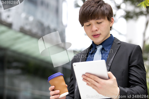 Image of Young Asian business executive in suit holding tablet and coffee