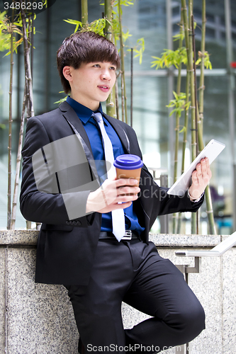 Image of Young Asian business executive in suit holding tablet and coffee