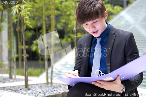 Image of Young Asian business executive in suit holding file